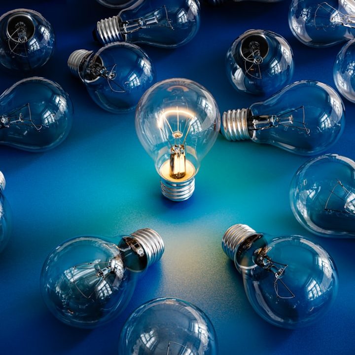Die zündende Idee Eine einzelne Glühbirne leuchtet unter vielen unbeleuchteten Glühbirnen auf einem blauen Hintergrund.